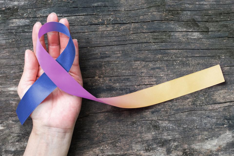 Main tenant un ruban bleu et violet contre le cancer