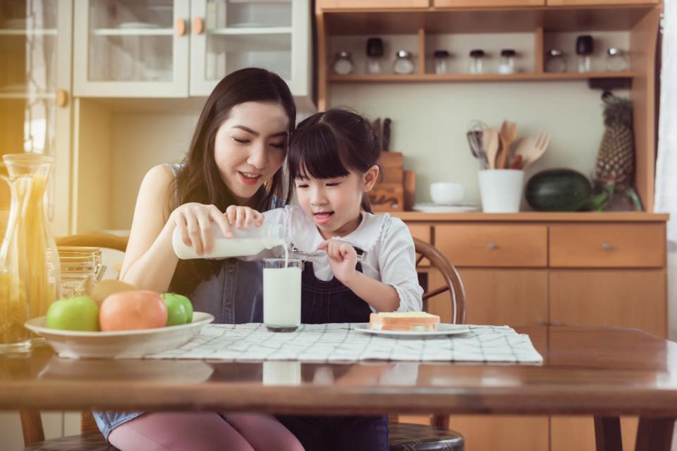 Une mère aide sa fille à verser soigneusement son lait dans un verre.