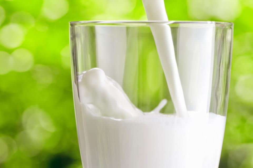 Milk being poured into a glass with green tree background