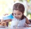 Petite fille versant soigneusement du lait dans son verre